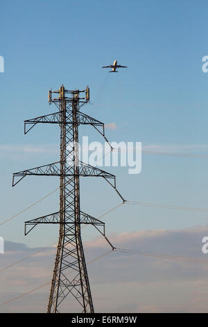 Ein Flugzeug fliegt über einen elektrischen Sendeturm. Stockfoto