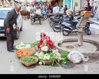 Straßenszene in Deogarh, Rajasthan, Indien: junge Frau im Sari sitzen auf der Straße verkauft frisches Gemüse an Passanten Stockfoto