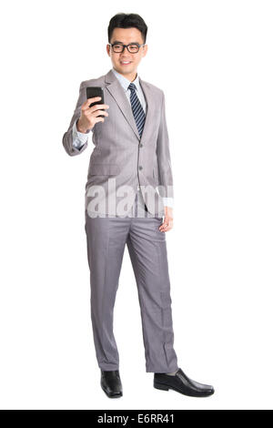 Ganzkörper von jungen asiatischen Geschäftsmann mit Smartphone, SMS und Blick auf das Telefon mit einem Lächeln auf seinem Gesicht, isolierte o Stockfoto