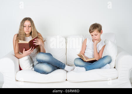 Jungen und Mädchen auf der Couch sitzen und ein Buch lesen Stockfoto