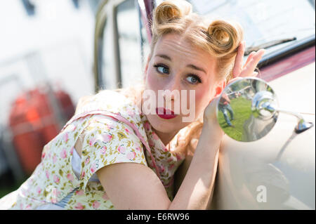 Eine Frau gekleidet in Retro-50er Jahre amerikanische Hausfrau Stil Sommer Kleid Kleid Anpassung überprüfen ihr Haar in einem Auto Außenspiegel Stockfoto