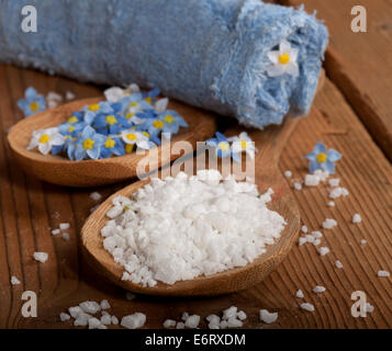 Spa-Hintergrund mit Meersalz in Holzlöffel, Blumen und gerollten Handtuch auf hölzernen Hintergrund. Stockfoto