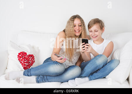 Jungen und Mädchen sitzen auf der Couch mit Ihrem Handy Stockfoto