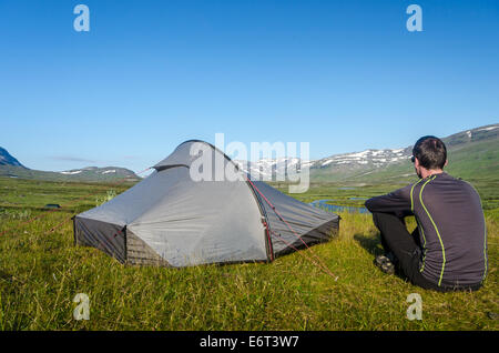 Ein Mann sitzt allein in der Nähe seines Zeltes in den Bergen auf dem Kungsleden (Königs Trail), im schwedischen Lappland Stockfoto