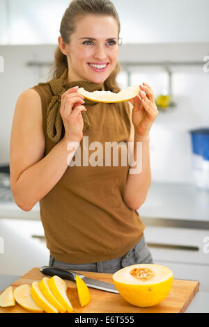 Glückliche junge Frau Essen Melone in Küche Stockfoto