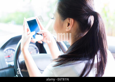 Junge Asiatin SMS-Nachricht auf Ihr Handy oder Smartphone während der Fahrt Auto Stockfoto