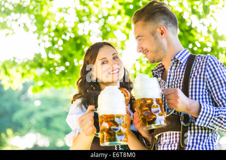 Deutsches Ehepaar in Tracht, die Bier trinken, im Schatten der Bäume Stockfoto