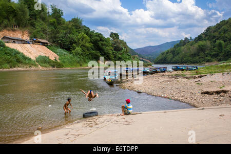 Flussschiffe und Kinder auf dem Nam Ou River, auf dem Dorf von Muang Ngoi Neua (auch genannt Ban Ngoi Kao) in Nordlaos. Stockfoto