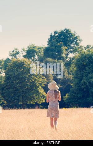 Eine junge Frau, die zu Fuß in ein Feld des Grases im Hyde Park, London im englischen Sommer Stockfoto