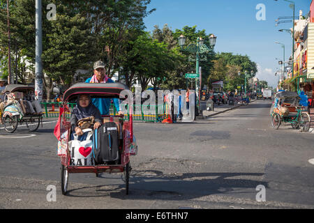 Yogyakarta, Java, Indonesien.  Frau Reiten in einem Becak, ein dreirädriges Fahrzeug von menschlichen Antrieb angetrieben.  Jalan Malioboro St. Stockfoto