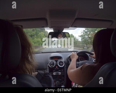 Ein Blick aus dem Rücksitz eines Autos mit einem Fahrer und Beifahrer auf einer ländlichen Straße unterwegs Stockfoto