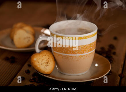 Tasse mit Kaffee, heiße Schokolade, Cappuccino, Latte oder Mochaccino und Gebäck in Form eines Herzens auf einem hölzernen Hintergrund. Stockfoto