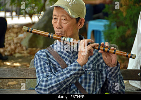 Einem älteren chinesischen Mann das Flötenspiel und Hereinholen Spenden im Columbus Park in Chinatown in New York City. Stockfoto