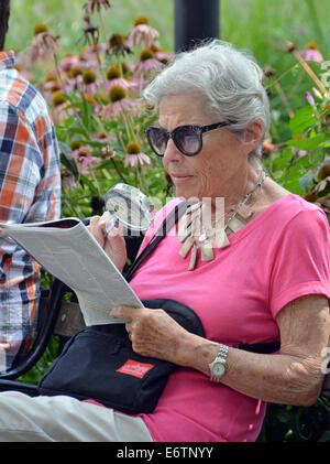 Eine ältere Frau, die New Yorker Magazin im Washington Square Park in New York City mit Hilfe einer Lupe zu lesen Stockfoto