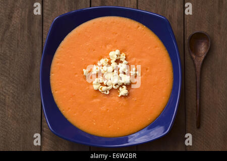 Ecuadorianische Tomate und Kartoffel Creme Suppe serviert mit Popcorn an der Spitze in einen blauen tiefen Teller mit einem Holzlöffel auf der Seite Stockfoto