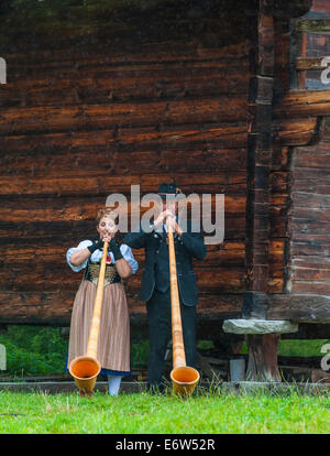 Ein Schweizer Mann und Frau Team von Alphornbläser ausführen außerhalb eine Holzhütte in den Berg Stadt von Nendaz Stockfoto