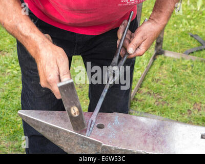 Nahaufnahme von einem Schmied bei der Arbeit, ein Stück rote heiße Eisen in Form auf einem Amboss Hämmern Stockfoto