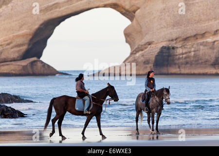 Reiten entlang Wharariki Beach in der Nähe von Farewell Spit, Torbogen Inseln im Hintergrund, Südinsel, Neuseeland Stockfoto