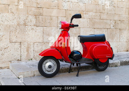 Vespa 50, roter Roller mit Helm parkte vor einer Wand, Alberobello, Apulien, Italien Stockfoto