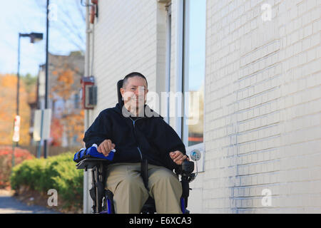 Mann mit Verletzungen des Rückenmarks und Arm mit Nervenschäden in motorisierten Rollstuhl mit einer öffentlichen Straße Stockfoto