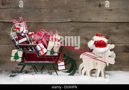 Weihnachtskarte-Dekoration: Elche Santa ziehen Schlitten mit Geschenken auf einem hölzernen Hintergrund - lustige Grußkarte im Landhausstil Stockfoto