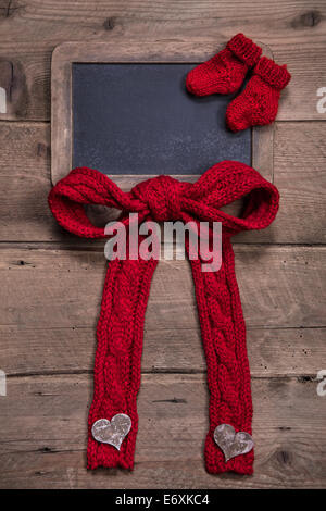 Tafel mit roten Gestrickte Socken und Bogen auf hölzernen Hintergrund für Geburtstag oder Geburt Stockfoto