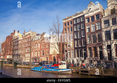 AMSTERDAM, Niederlande - 19. März 2014: Bunte Häuser entlang des Kanals in sonnigen Frühlingstag. Gewöhnliche Menschen Fuß an der Küste Stockfoto