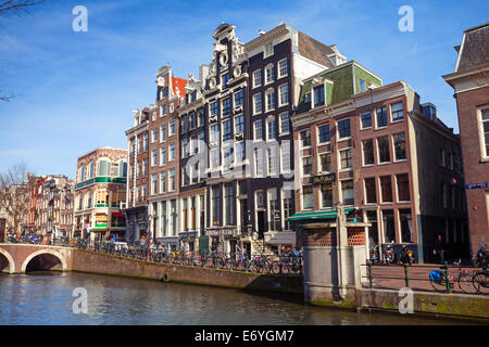 AMSTERDAM, Niederlande - 19. März 2014: Bunte Häuser auf dem Kanal-Damm in sonnigen Frühlingstag. Normale Menschen gehen Stockfoto