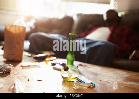 Mann ließ sich auf Sofa mit Drogen-Utensilien im Vordergrund Stockfoto