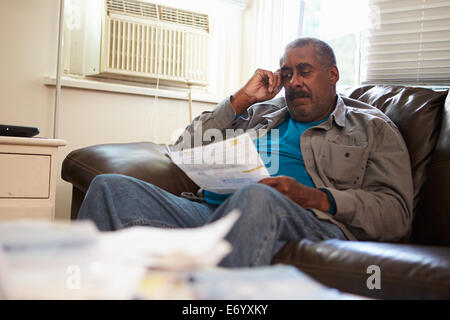 Besorgt Senior Mann auf Sofa Blick auf Rechnungen Stockfoto