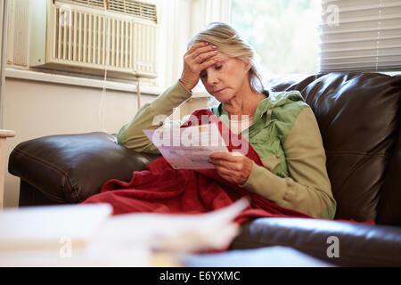 Besorgt Senior Woman Sitting On Sofa Blick auf Rechnungen Stockfoto