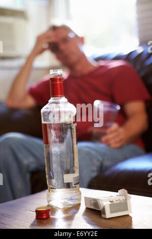Mann sitzt auf dem Sofa mit Flasche Wodka und Zigaretten Stockfoto