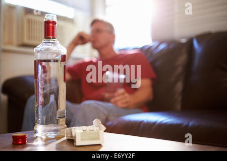 Mann sitzt auf dem Sofa mit Flasche Wodka und Zigaretten Stockfoto