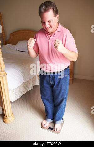 Glücklich übergewichtiger Mann stehend auf Skalen im Schlafzimmer Stockfoto
