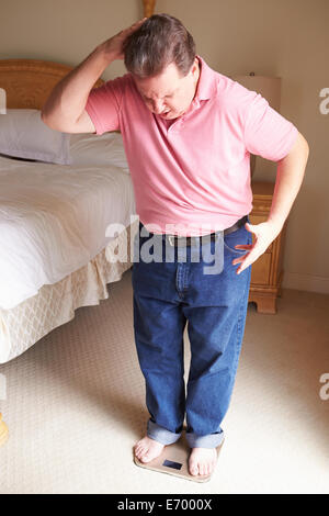 Übergewichtiger Mann wiegen sich auf Skalen im Schlafzimmer Stockfoto