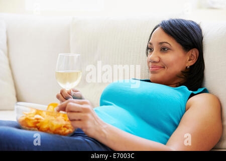 Übergewichtige Frau zu Hause essen Chips und trinken Wein Stockfoto