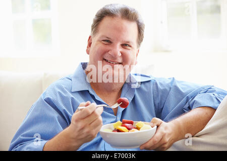 Übergewichtigen Sie Mann sitzt auf dem Sofa, die Schale mit frischem Obst essen Stockfoto