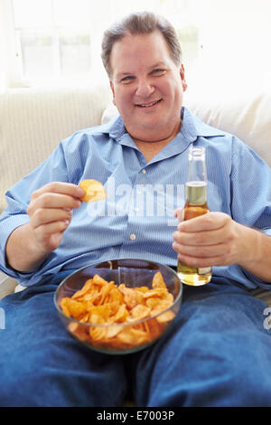 Übergewichtiger Mann zu Hause essen Chips und Bier zu trinken Stockfoto