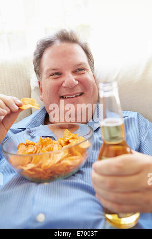 Übergewichtiger Mann zu Hause essen Chips und Bier zu trinken Stockfoto