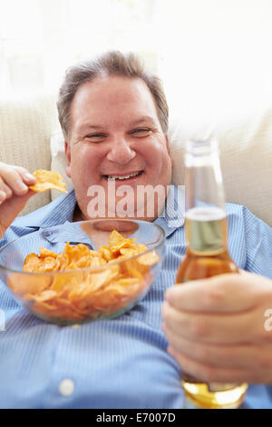 Übergewichtiger Mann zu Hause essen Chips und Bier zu trinken Stockfoto