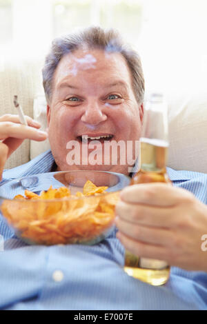 Übergewichtige Menschen essen Chips, Bier trinken und Rauchen Stockfoto