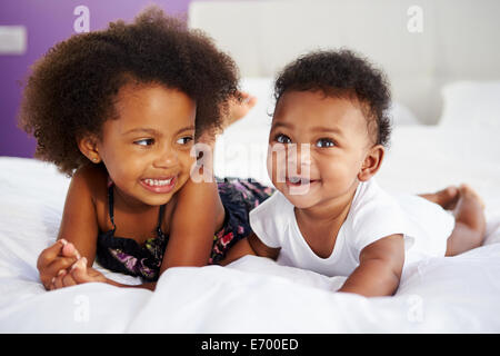 Schwester mit Bruder liegend im Bett der Eltern Stockfoto