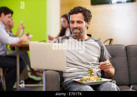 Mann auf Sofa sitzen und Essen im Designstudio Stockfoto
