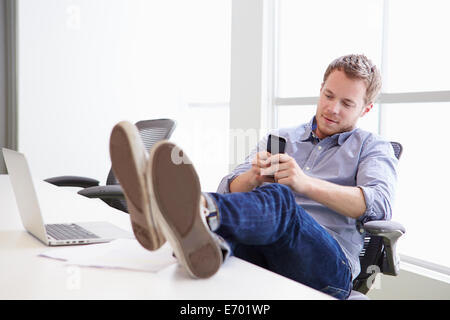 Mann mit Handy am Schreibtisch im Designstudio Stockfoto