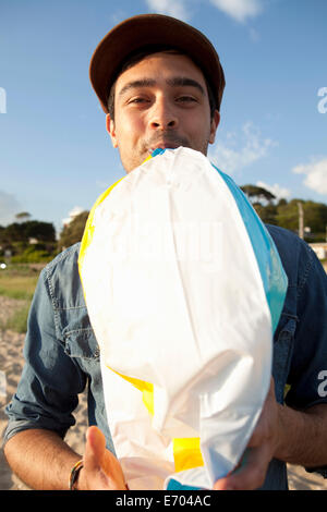 Junger Mann Sprengung Beach Ball am Strand von Bournemouth, Dorset, Großbritannien Stockfoto