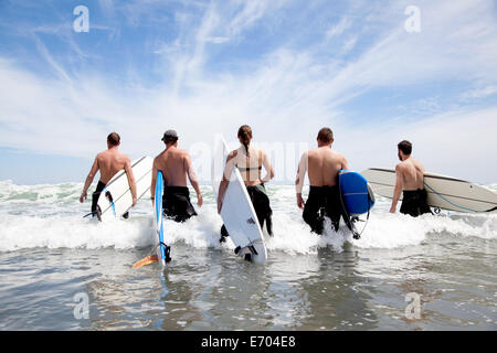 Rückansicht einer Gruppe von männlichen und weiblichen Surfer Freunde waten in Meer mit Surfbrettern Stockfoto