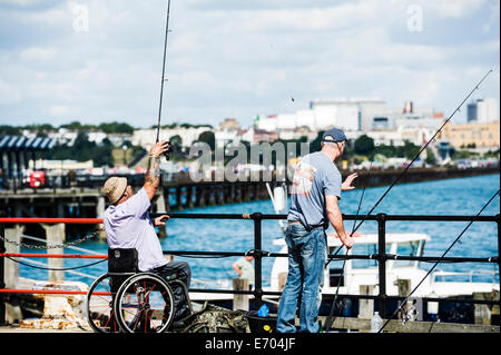 Behinderte Menschen in einem Rollstuhl Angeln von einem Pier. Stockfoto