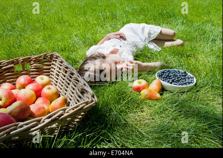 Mädchen schlafend auf dem Rasen mit Korb mit Äpfeln und Birnen Stockfoto