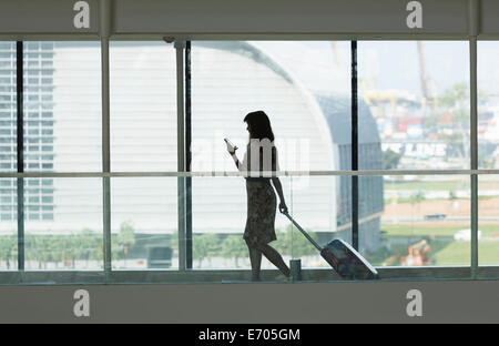 Junge Frau mit Smartphone und ziehen Koffer im Flughafen Stockfoto
