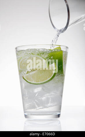 Klarem Wasser eingießen von Krug in Trinkglas mit Kalk und Eiswürfeln Stockfoto